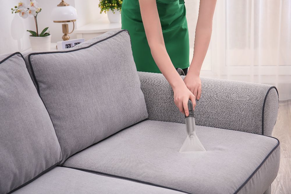 Woman cleaning couch with vacuum cleaner home (1)